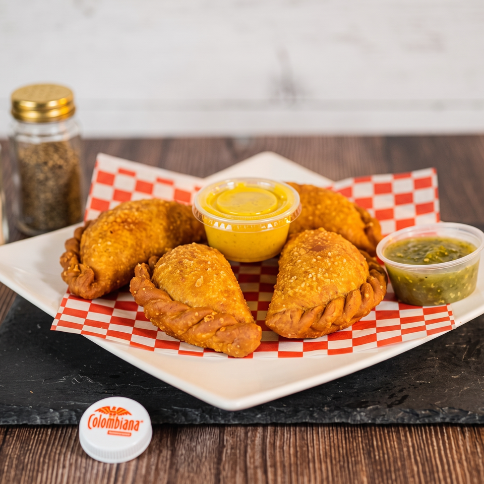A plate of golden-brown empanadas with two dipping sauces, salt, and pepper shakers.