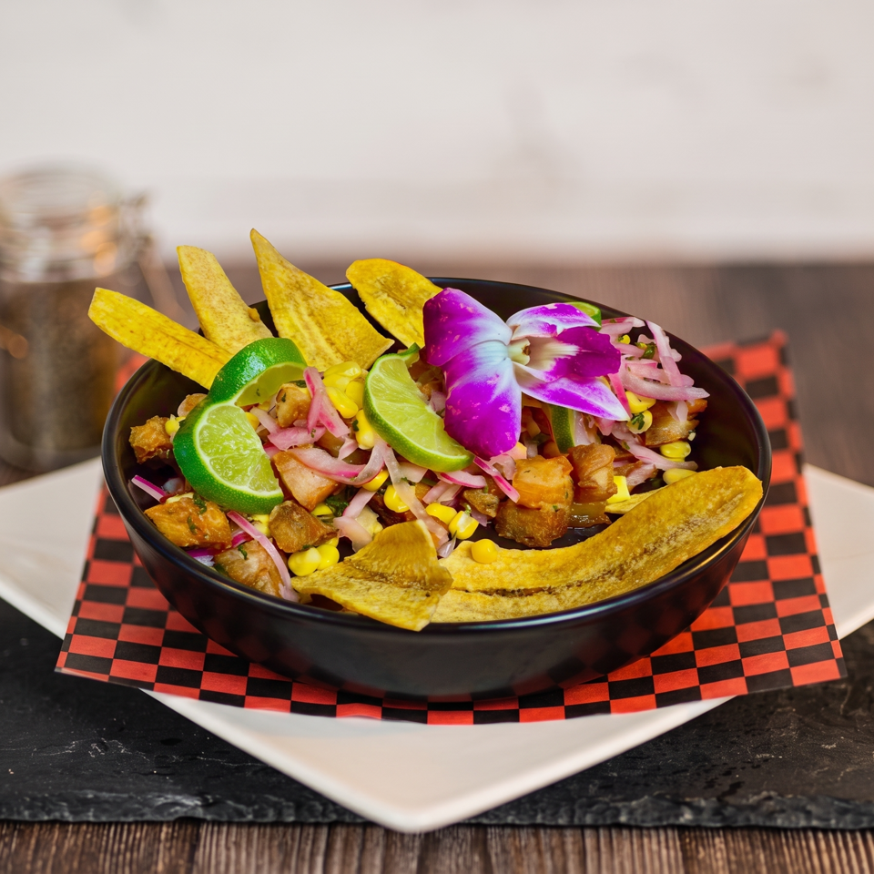 A colorful ceviche dish with plantain chips, lime, corn, and a purple orchid garnish.